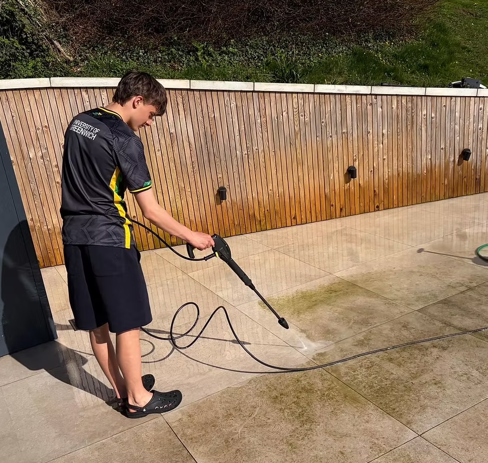 Professional power washing operative cleaning stone patio pavers in a residential garden with jet wash equipment